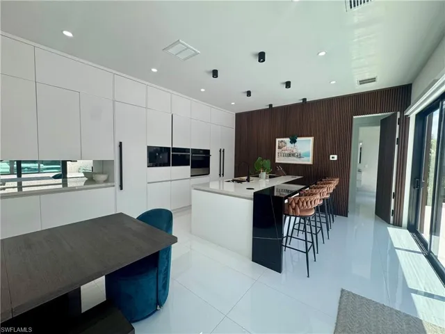 Contemporary kitchen featuring an expansive center island with an integrated breakfast bar, white flat-panel cabinetry, built-in appliances, recessed lighting, and large format white tile flooring