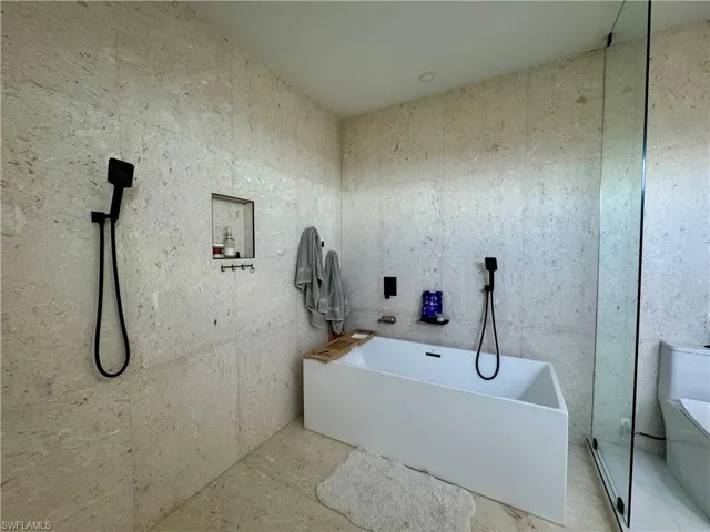 Freestanding soaking tub with matte black fixtures, full-height stone-look tile, and a glass-enclosed shower area