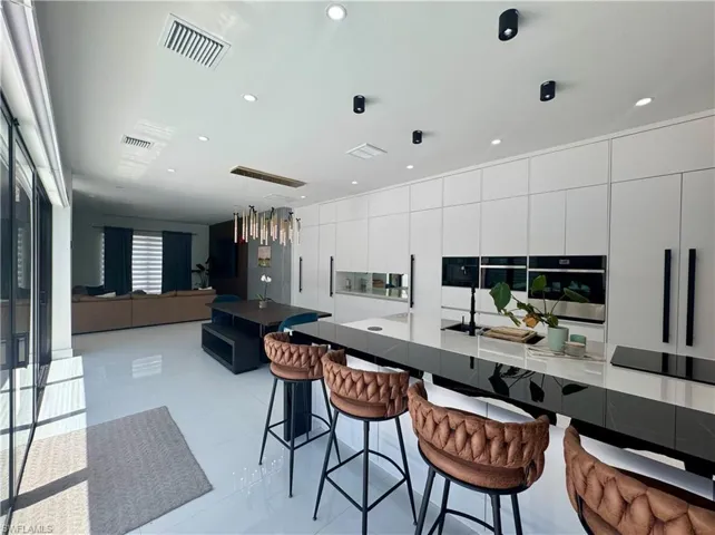 Modern kitchen featuring a large waterfall island with integrated cooktop, white flat-panel cabinetry, built-in wall ovens, and recessed lighting