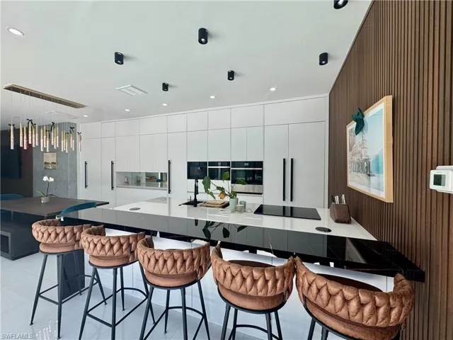 Modern kitchen featuring an expansive island with a waterfall countertop, integrated cooktop, and a black sink