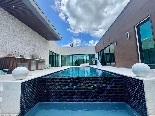 Contemporary outdoor living area featuring a rectangular pool with dark subway tile, an outdoor kitchen with built-in appliances, and a wood-slat accent wall
