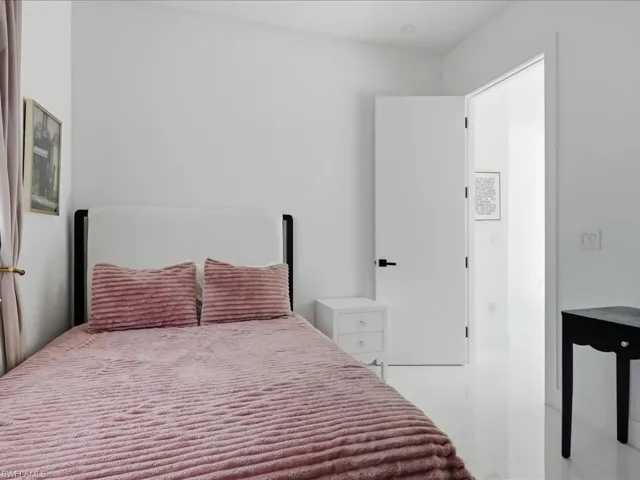 Room featuring bright white walls, white glossy flooring, a white headboard, a white nightstand, and a white interior door with matte black hardware