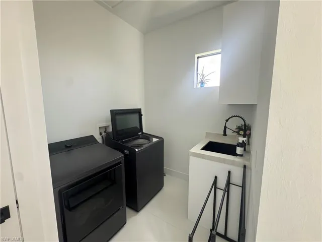 Laundry area featuring a built-in sink with a black faucet, white cabinetry, and a window for natural light