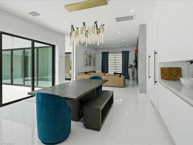 Contemporary dining area with a linear chandelier, large format white tile flooring, and sliding glass doors