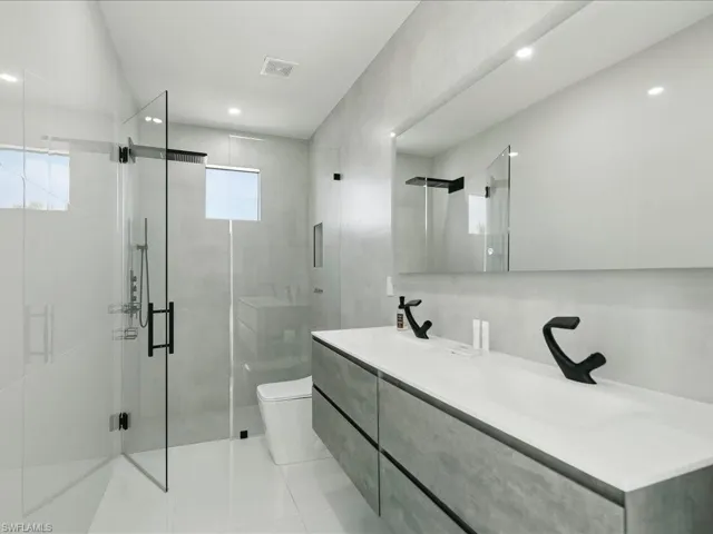 Modern bathroom featuring a double vanity with matte black faucets, a frameless mirror, and recessed lighting