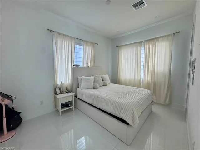 White tile flooring, two window openings with curtain rods, crown molding, and a built-in ceiling vent