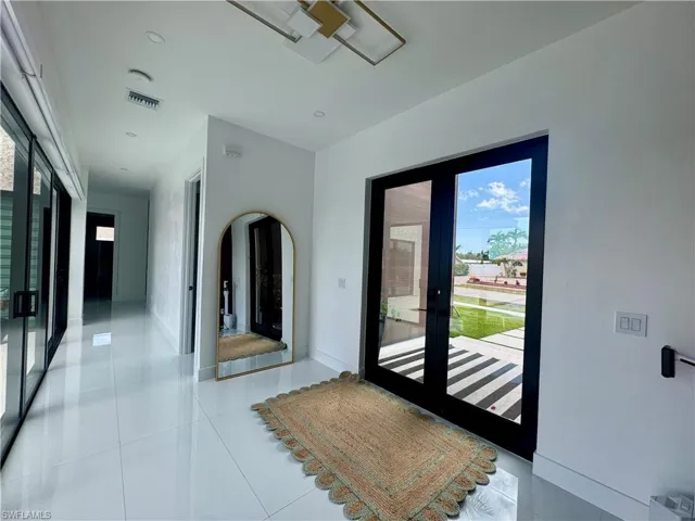 Bright entryway featuring double glass doors, white tile flooring, recessed lighting, and a modern ceiling fixture