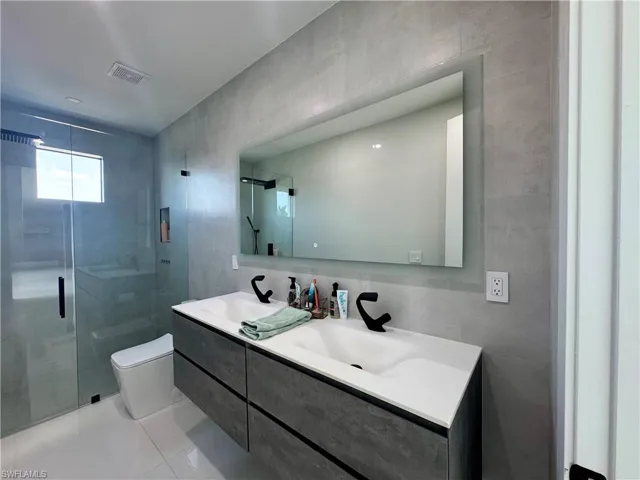Contemporary bathroom featuring a floating double vanity with integrated sinks, matte black faucets, a frameless mirror, and a glass-enclosed shower with a rainfall showerhead