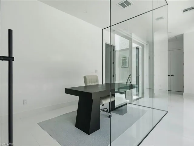 Glass-enclosed office space featuring a minimalist black desk, white walls, and light-toned flooring