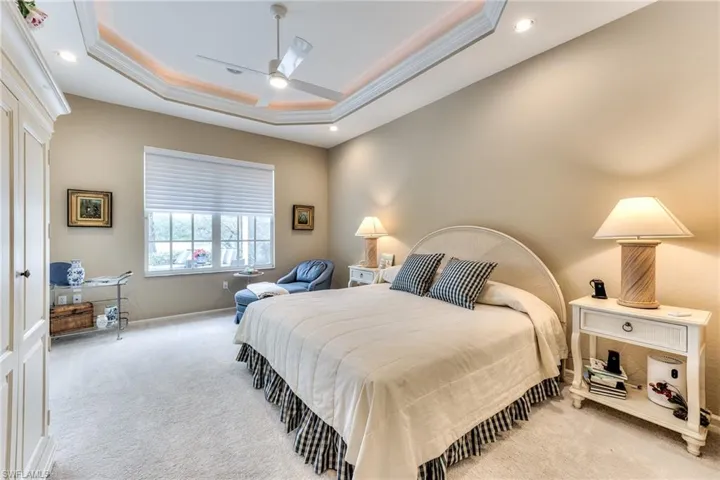 Carpeted bedroom featuring a raised ceiling, ceiling fan, and ornamental molding