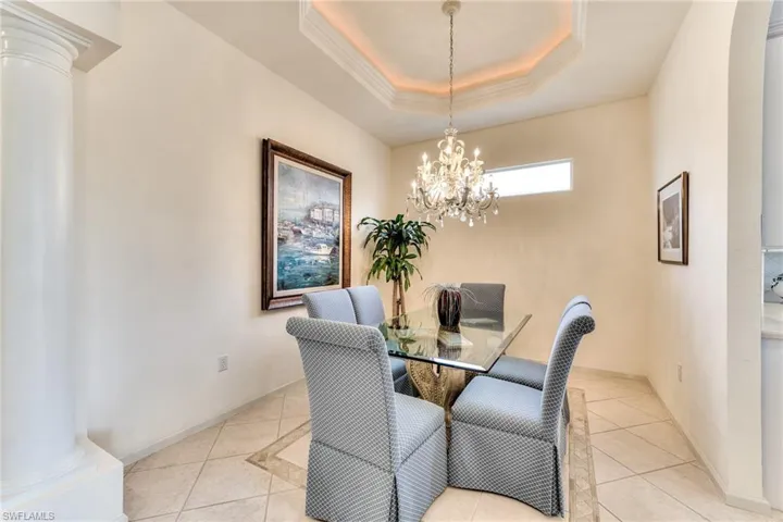 Tiled dining space featuring a raised ceiling, an inviting chandelier, and decorative columns