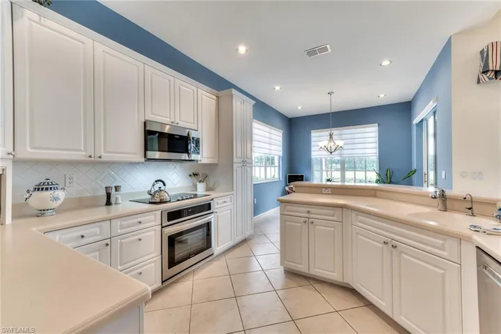 Kitchen with decorative backsplash, appliances with stainless steel finishes, a chandelier, and white cabinetry