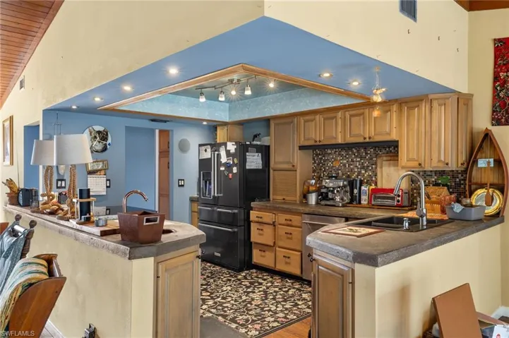 Kitchen with sink, decorative backsplash, track lighting, kitchen peninsula, and black refrigerator with ice dispenser