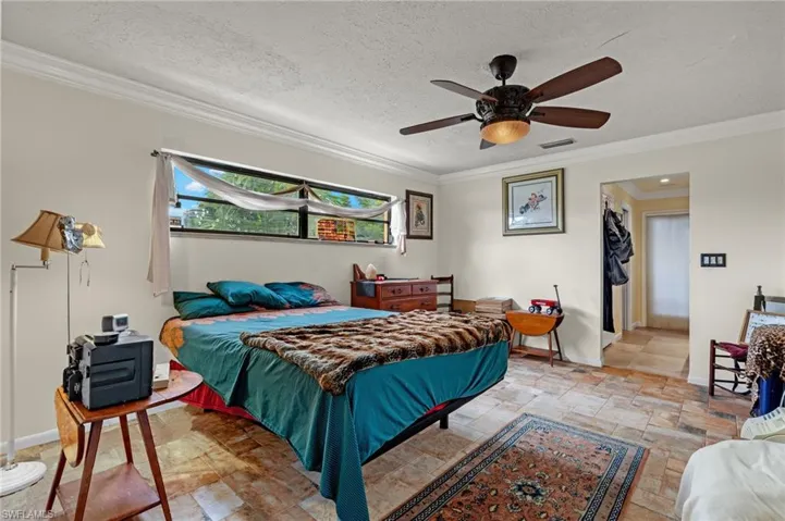 Tiled bedroom featuring a textured ceiling, ceiling fan, and ornamental molding