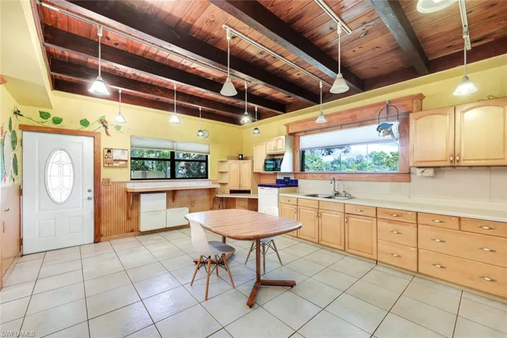 Kitchen featuring light brown cabinetry, beam ceiling, wood ceiling, tile floor, hanging light fixtures, white appliances and sink