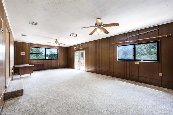 Carpeted empty bonus room with wood burning fireplace, wood-paneling walls, ceiling fan, and a textured ceiling