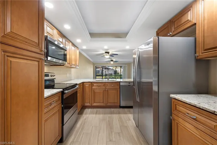 Kitchen featuring brown cabinets, ornamental molding, stainless steel appliances, a tray ceiling, and light stone counters