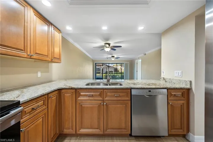 Kitchen featuring brown cabinetry, crown molding, light stone countertops, appliances with stainless steel finishes, and ceiling fan