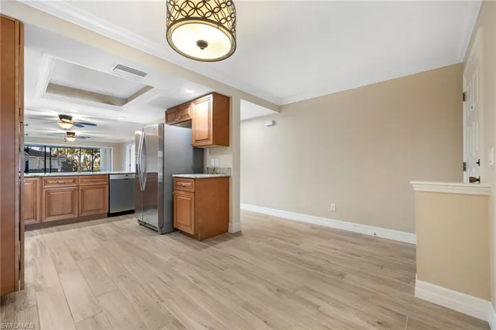Kitchen with brown cabinetry, light wood-style floors, ornamental molding, stainless steel appliances, and a raised ceiling