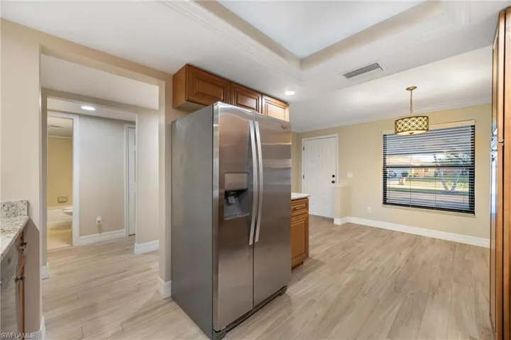 Kitchen with stainless steel fridge with ice dispenser, brown cabinets, light wood-style floors, decorative light fixtures, and a tray ceiling