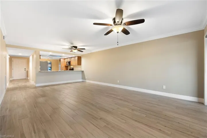Unfurnished living room featuring crown molding, light wood finished floors, and a ceiling fan