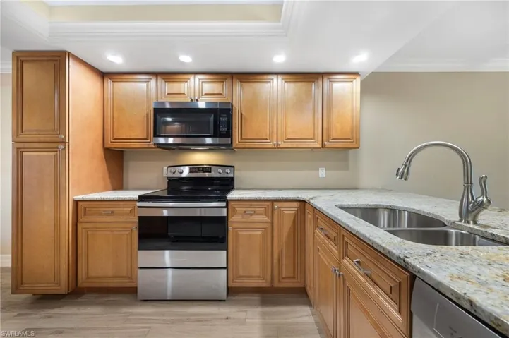 Kitchen featuring light stone countertops, appliances with stainless steel finishes, recessed lighting, ornamental molding, and brown cabinets