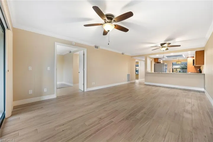 Unfurnished living room featuring ornamental molding, light wood-style flooring, and a ceiling fan