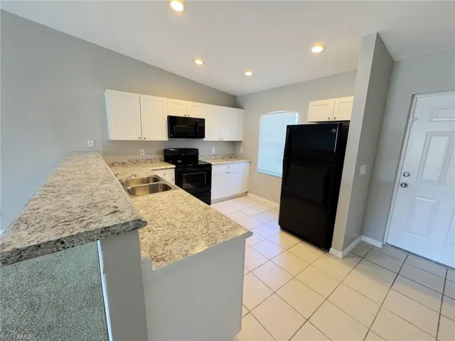 Kitchen featuring kitchen peninsula, white cabinetry, sink, and black appliances