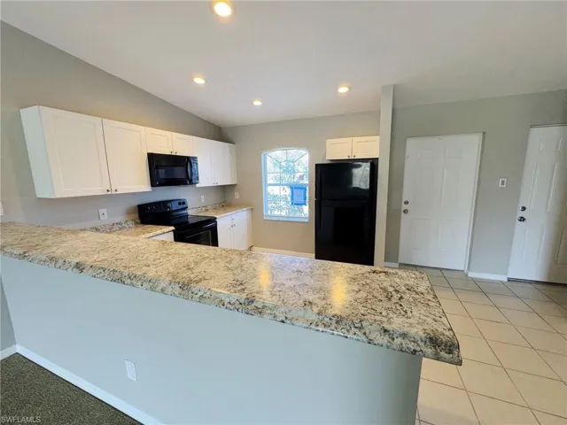 Kitchen featuring white cabinetry, kitchen peninsula, lofted ceiling, light tile patterned floors, and black appliances