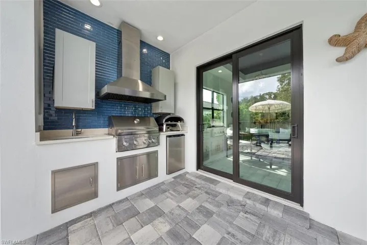 Kitchen with stainless steel fridge, decorative backsplash, white cabinetry, wall chimney exhaust hood, and sink