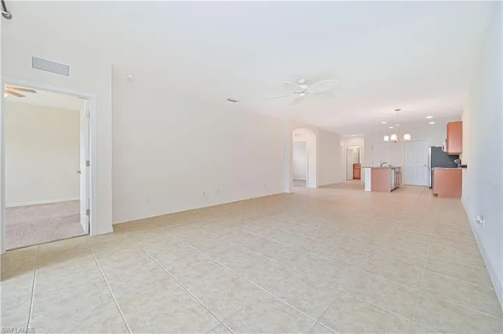 Unfurnished living room featuring a chandelier, a ceiling fan, light tile patterned floors, and arched walkways