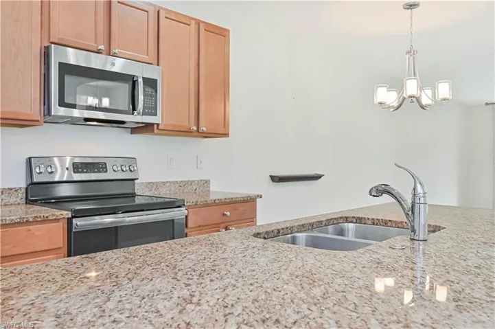 Kitchen with appliances with stainless steel finishes, a chandelier, light stone counters, and hanging light fixtures