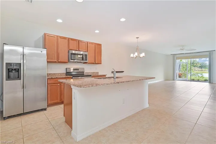 Kitchen featuring appliances with stainless steel finishes, light tile patterned floors, light stone counters, a chandelier, and open floor plan