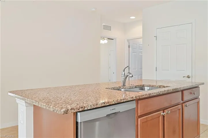Kitchen featuring dishwasher, an island with sink, light stone countertops, recessed lighting, and light tile patterned floors
