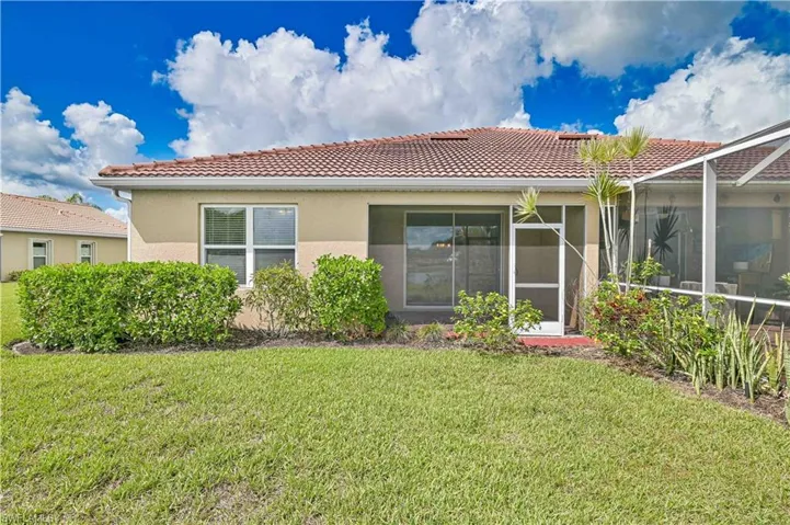 Rear view of property featuring a tile roof, a lawn, and stucco siding