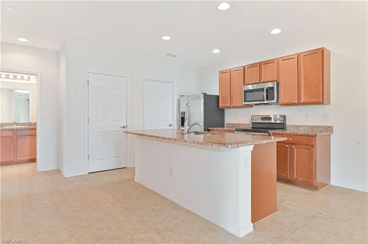 Kitchen featuring stainless steel appliances, an island with sink, light stone counters, light tile patterned floors, and recessed lighting