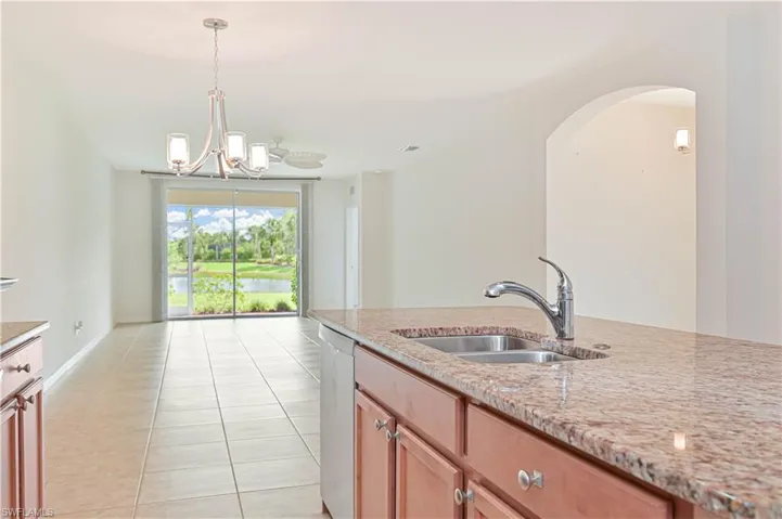 Kitchen with stainless steel dishwasher, light stone counters, light tile patterned flooring, hanging light fixtures, and arched walkways