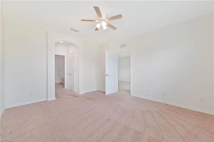 Empty room with arched walkways, ceiling fan, and light colored carpet