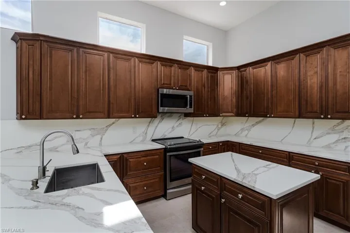 Kitchen with appliances with stainless steel finishes, light stone counters, dark brown cabinetry, tasteful backsplash, and a kitchen island