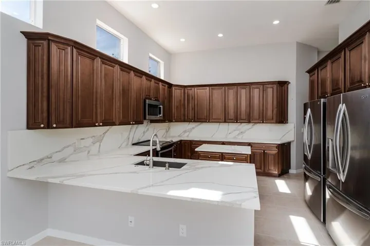 Kitchen with stainless steel appliances, dark brown cabinetry, a peninsula, light stone counters, and recessed lighting