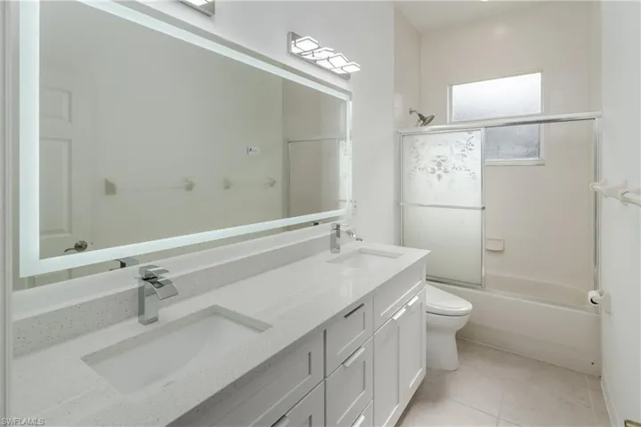 Full bath with double vanity, bath / shower combo with glass door, and light tile patterned flooring