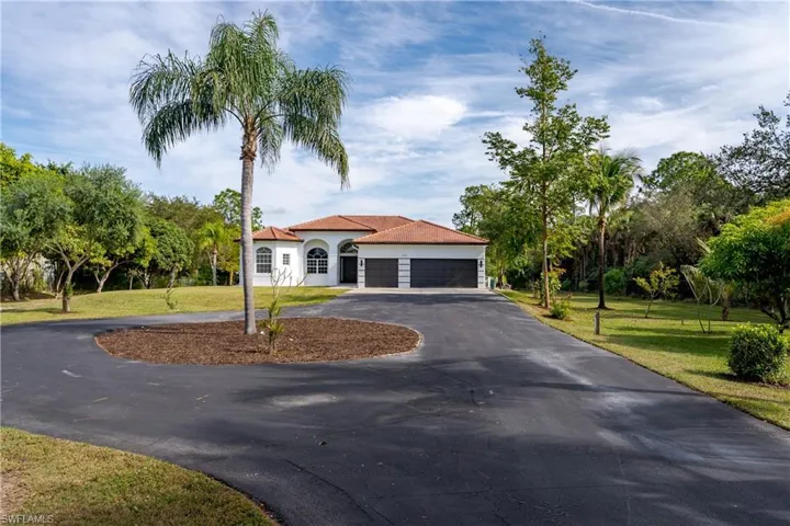 Mediterranean / spanish house featuring curved driveway, a front yard, an attached garage, stucco siding, and view of wooded area