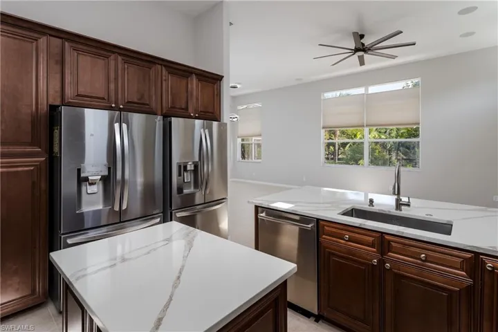 Kitchen with dark brown cabinetry, appliances with stainless steel finishes, light stone countertops, a center island, and a ceiling fan