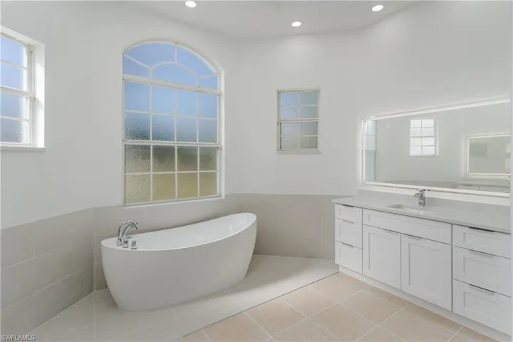 Bathroom featuring tile walls, a wainscoted wall, a soaking tub, vanity, and light tile patterned flooring
