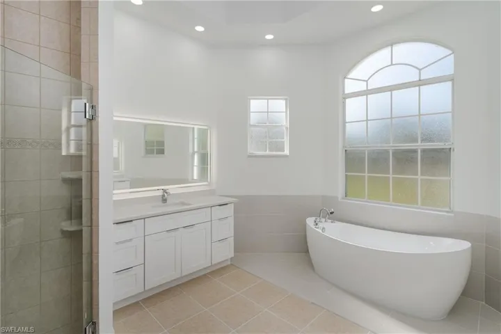 Full bathroom featuring tile walls, a wainscoted wall, a freestanding tub, vanity, and a stall shower