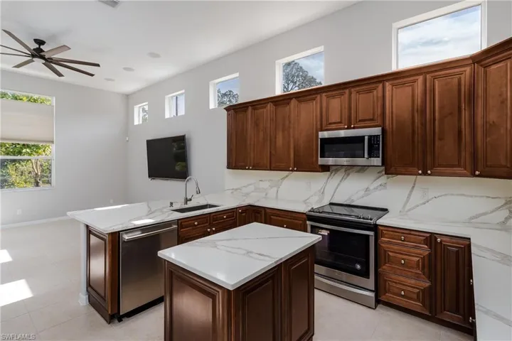 Kitchen featuring appliances with stainless steel finishes, a peninsula, backsplash, light stone countertops, and light tile patterned floors