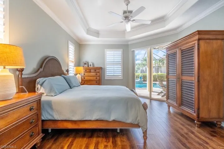 Bedroom featuring a tray ceiling, access to outside, crown molding, ceiling fan, and dark hardwood / wood-style floors