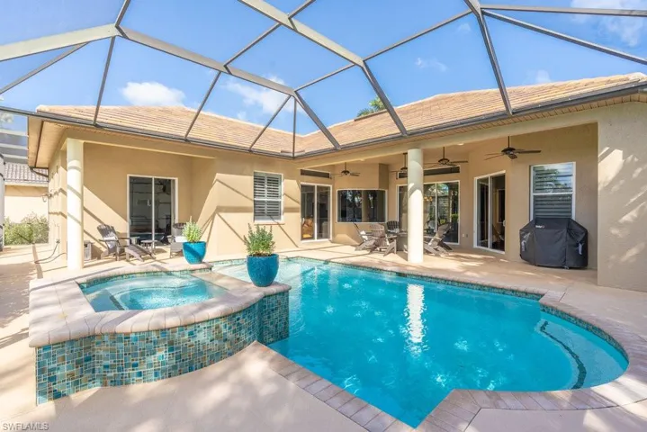 View of swimming pool with glass enclosure, ceiling fan, a patio area, area for grilling, and an in ground hot tub