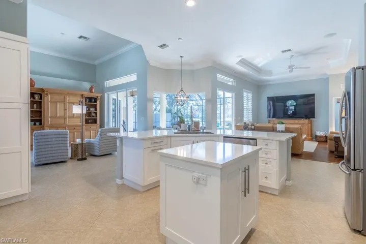 Kitchen featuring appliances with stainless steel finishes, ornamental molding, a center island, white cabinetry, and hanging light fixtures