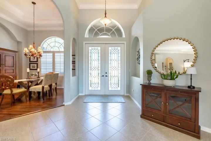 Foyer entrance with ornamental molding, french doors, a chandelier, and light wood-type flooring